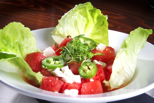 Watermelon cubes with crumbled white cheese and sliced jalapeño in a lettuce-lined bowl