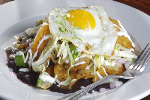 Fried egg on crisp tortilla chips with red beans, cream, shredded cabbage and pickled red onion