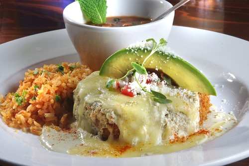 Cheese-topped stuffed item with cream sauce and avocado beside Spanish rice and a bowl of soup