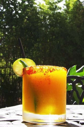 Orange cocktail with a chili-spiced rim, lime wheel and black straw on an outdoor table