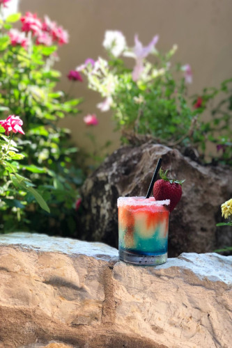 Layered red, yellow and blue cocktail with a sugared rim and strawberry on a stone ledge