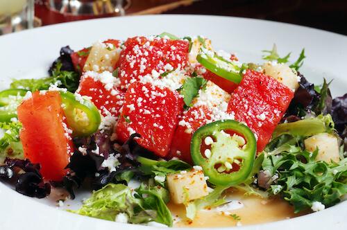 Watermelon salad with crumbled white cheese, jalapeño slices and cubed cheese over mixed greens