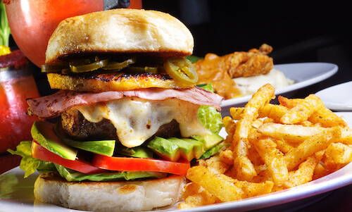 Burger with ham, melted cheese, jalapeño slices, avocado and tomato, served with seasoned french fries