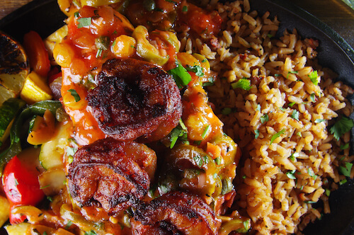 Close-up of grilled shrimp over sautéed peppers and onions, next to Spanish rice