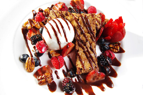Dessert plate with a scoop of ice cream, a pastry, mixed berries, pecans and chocolate drizzle