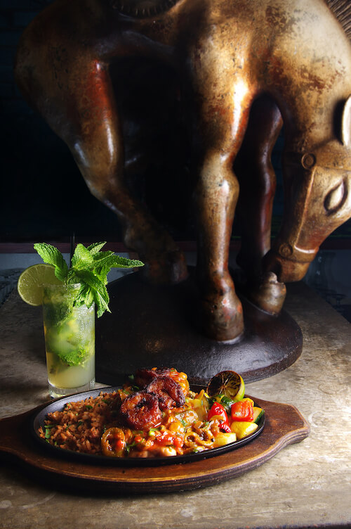 Skillet of rice, shrimp and vegetables with a mojito before a large bronze horse statue