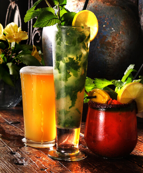 Pint of beer, a tall mint mojito and a chili-rimmed Bloody Mary on a wooden table