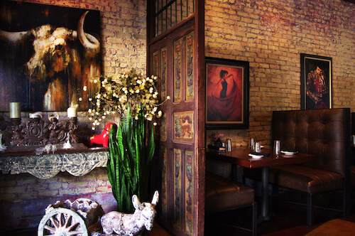 Dining room with brick walls, leather booths, a carved door and bull and dancer paintings