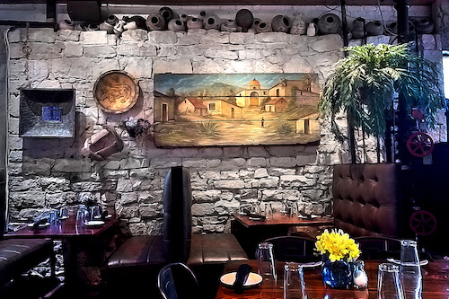 Dining room with a rough stone wall, a landscape painting, leather booths and yellow flowers