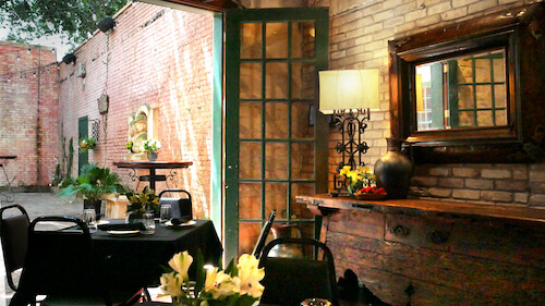 Table set with black linens by a green-framed glass door opening to a brick courtyard