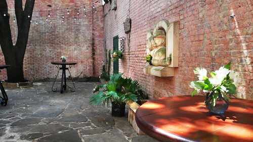 Brick courtyard patio with flagstone floor, a tree, string lights, a bistro table and palm