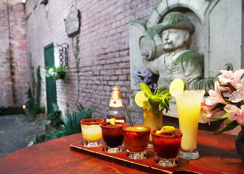 Beer bottle, a margarita and rimmed shot glasses on a tray by a stone statue